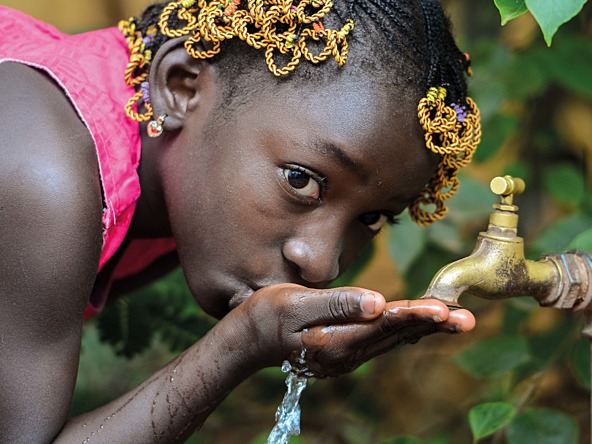young girl of African descent drinking water from a tap